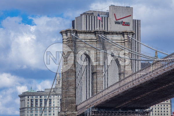 Brooklyn Bridge close-up with American flag and Verizon Building in background in NYC