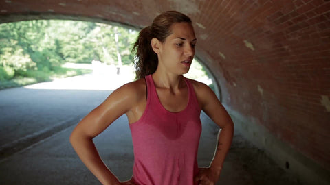 beautiful athlete taking break from exercise under Central Park bridge - attractive woman in pink tank top huffing and puffing after running