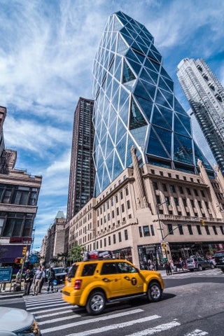caravan taxi cab driving in traffic past famous Hearst Building in Manhattan on bright sunny day