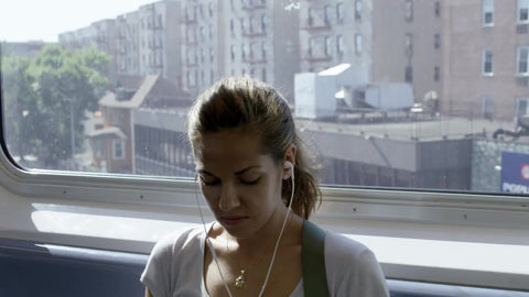 woman with earbuds on elevated train, pretty girl on subway riding through Queens with headphones