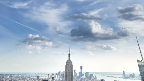 Empire State Building and Manhattan skyscrapers in cityscape tilting down from clouds overhead - day to night timelapse of NYC