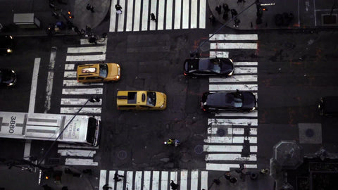 zooming out from overhead view of crosswalk street from tall building, cars driving in traffic in NYC