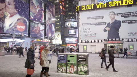 people walking past garbage and recycling bins in snow - snowing in Times Square at night