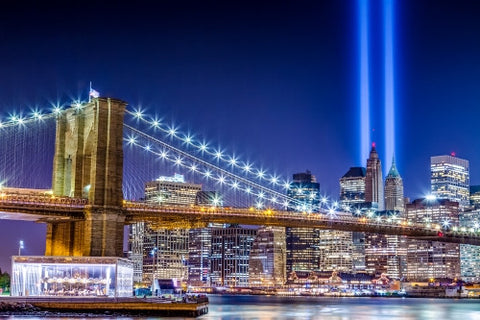 911 memorial lights, beams over Manhattan skyline with buildings and skyscrapers and Brooklyn Bridge lit up at night - carousel on East River