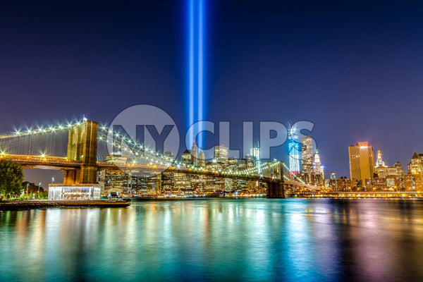 East River with 911 beams and Brooklyn Bridge reflecting off water, Manhattan skyline in background at night