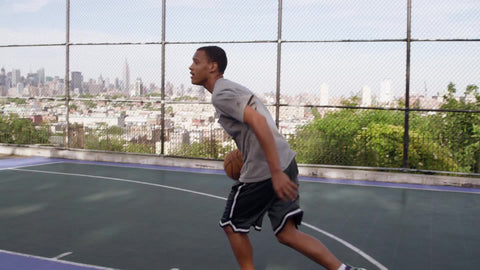 teenager dribbling up to basket and scoring layup - New Jersey basketball court overlooking Manhattan skyline through fence
