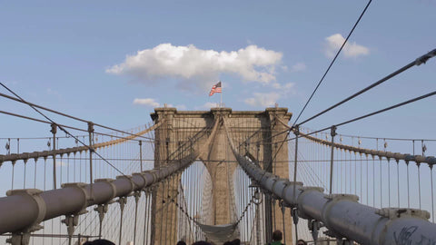 American flag at top of Brooklyn Bridge tower on beautiful blue sky day, people walking below