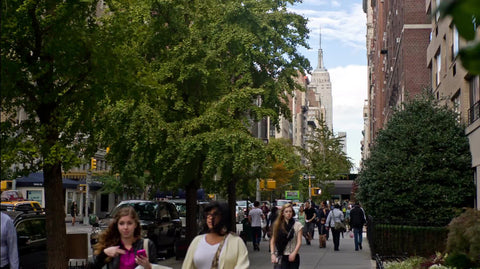 windy early summer day on Lower 5th Ave with NYU students walking - people enjoy end of spring - Empire State Building street view