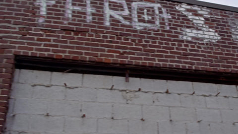 driving past gritty low red brick buildings in Brooklyn with vandalism and graffiti