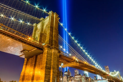 Brooklyn Bridge at night with 911 beams over Manhattan skyline, upward angle under beautiful evening sky with lights