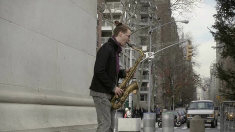 man playing saxophone under Washington Square Park arch in Manhattan with view of Empire State Building in background