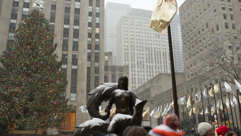 panning past Christmas tree at Rockefeller Center, tilting down to ice skating rink - snowing in winter NYC