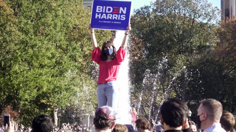 girl holding Biden Harris sign over head in Washington Square Park in NYC