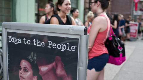 women waiting on line for Yoga with people in background and sign in front on summer day in East Village NYC
