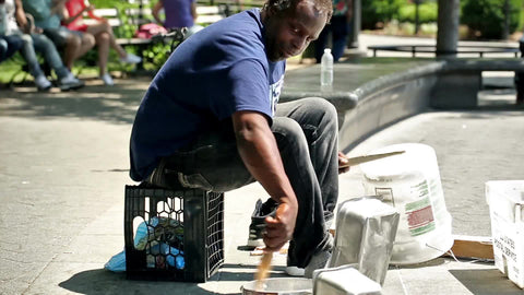 drummer sitting on milk crate in Washington Square Park banging on pots and pans - talented street performer in summer in NYC