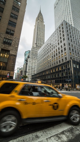 yellow caravan taxi cab driving past Chrysler Building skyscraper in Midtown Manhattan