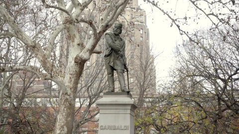 man playing saxophone under Garibaldi statue in Washington Square Park on fall day
