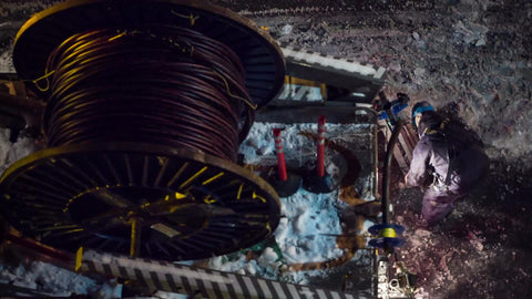 spool of fiber optic cables overhead view construction worker - man in hardhat working at night in street in winter snow - snowing