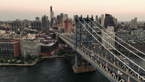 aerial turning from Brooklyn to Manhattan skyline with cars driving across bridge at sunset New York City