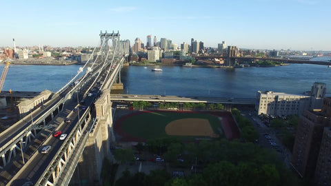aerial pulling back from Manhattan Bridge on bright sunny day with baseball field on Eastside
