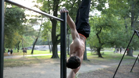man bracing body on side with Central Park pull-up bar on summer day