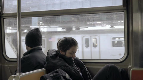 woman and man riding subway back to back - strangers on B Train crossing Manhattan Bridge on winter day in NYC