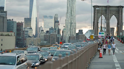 Freedom Tower view from Brooklyn Bridge with tourists walking across and cars driving in traffic on summer day in NYC