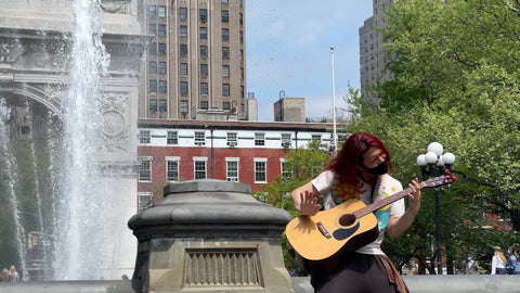 musician with long hair playing acoustic guitar by fountain in Washington Square Park in New York City NYC