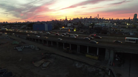 high view of cars driving in traffic on the highway with beautiful Manhattan skyline at sunset
