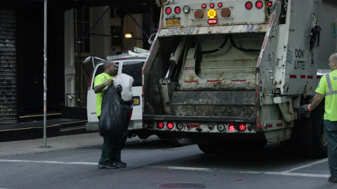 sanitation workers dumping trash in back of garbage truck in slow motion on summer day in SoHo Downtown Manhattan