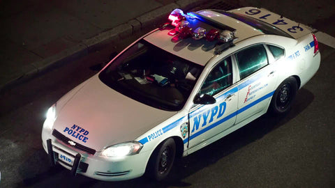 NYPD police car with flashing turret lights double parked in street at night with tourism bus driving by
