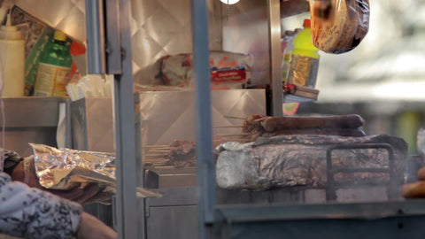 hot dog vendor serving customer at smoky cart - closeup squeezing ketchup and mustard - street food in NYC