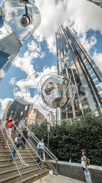 upward angle of Columbus Circle with famous globe sculpture and people in Midtown Manhattan on sunny summer day from subway station stairs in NYC