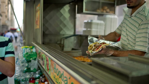man wrapping falafel at Halal food truck and serving customer outside in summer