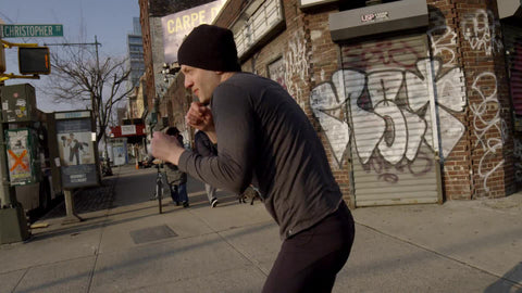man shadow boxing in street - throwing punches on westside of Manhattan with graffiti on building