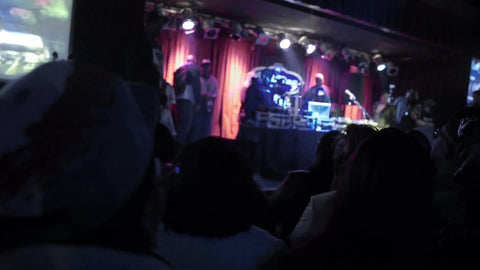 performers onstage at hip hop show under bright lights - heads bobbing in audience