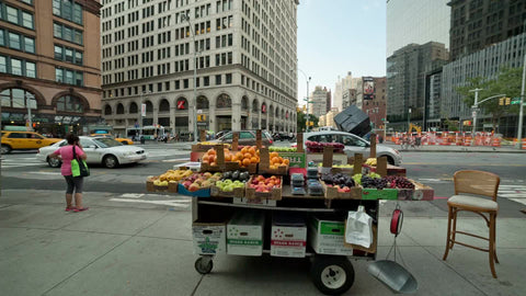 fruit stand in Cooper Square on summer day with famous cube sculpture in background