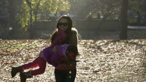 mother spinning her daughter around in circles in leafy fall meadow with changing colorful leaves on ground, slow motion Central Park 4K
