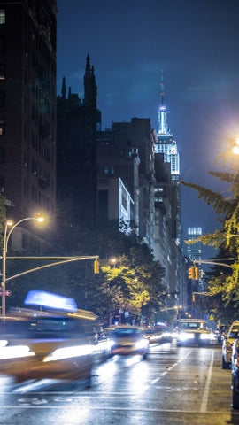Empire State Building with blur motion taxi cabs driving down Lower Fifth Ave at night in Manhattan