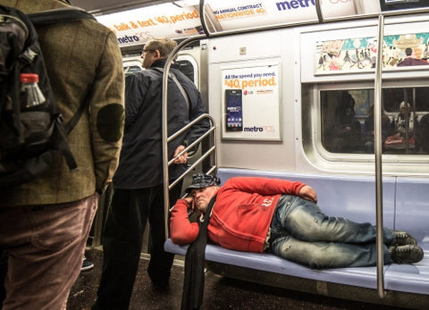 homeless man sleeping on subway train seats, taking up whole bench