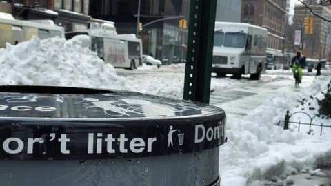bicyclist riding bicycle on snow in winter with do not litter trash can in New York City NYC