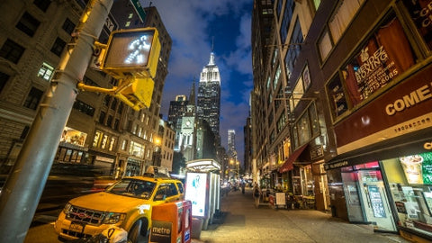 Lower 5th Ave at night with Empire State Building and walk light and parked caravan taxi cab