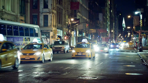 taxicabs driving down Broadway at night with Chrysler Building in background in NYC