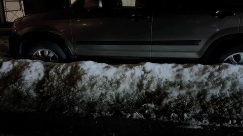 tracking shot driving past piles of snow on ground in street by parked cars cold winter