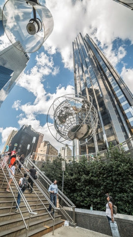 upward angle of Columbus Circle with famous globe sculpture and people in Midtown Manhattan on sunny summer day from subway station stairs in NYC