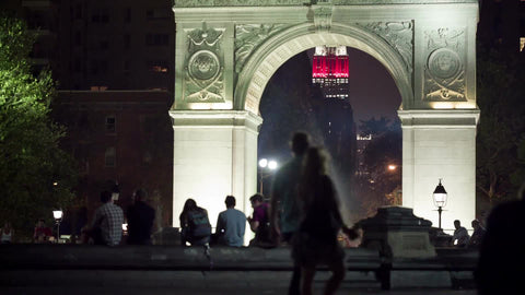 Washington Square Park arch at night with view of Empire State Building lights and young people hanging out in NYC