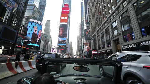 woman in convertible driving through Times Square on cloudy summer day