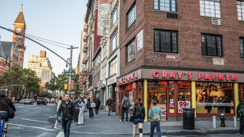 Gray's Papaya on corner of 8th Street and 6th Ave in Greenwich Village with Jefferson Market Library clock tower in late afternoon fall day