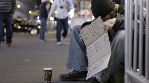 homeless man holding sign at night on street off Times Square on sold fall night