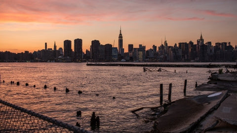 Manhattan skyline with Empire State Building silhouette view from Brooklyn across East River with wood dowels in water - early evening pink orange and purple sunset in NYC